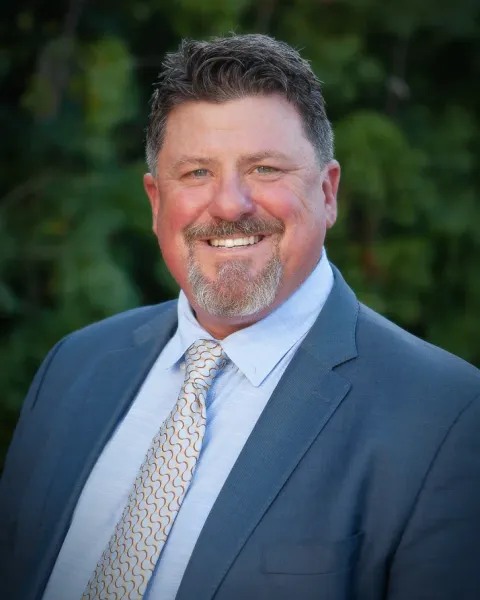 Portrait of Darin Andersen, smiling, in a blue suit and patterned tie, outdoors