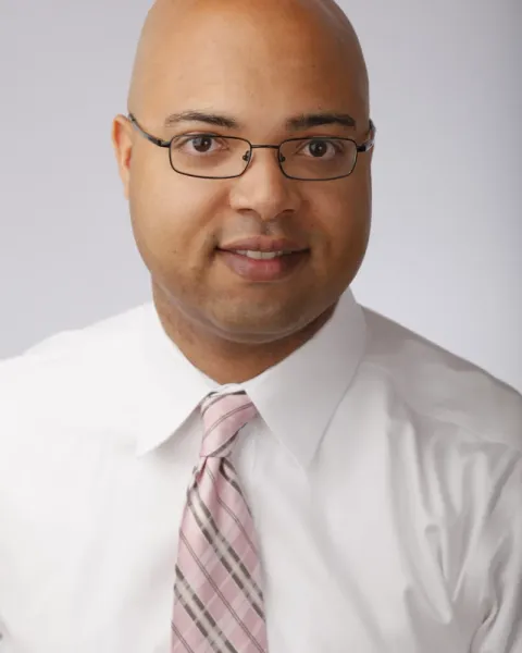 Portrait of Erik Caldwell, smiling, wearing glasses, a white shirt and a pink plaid tie