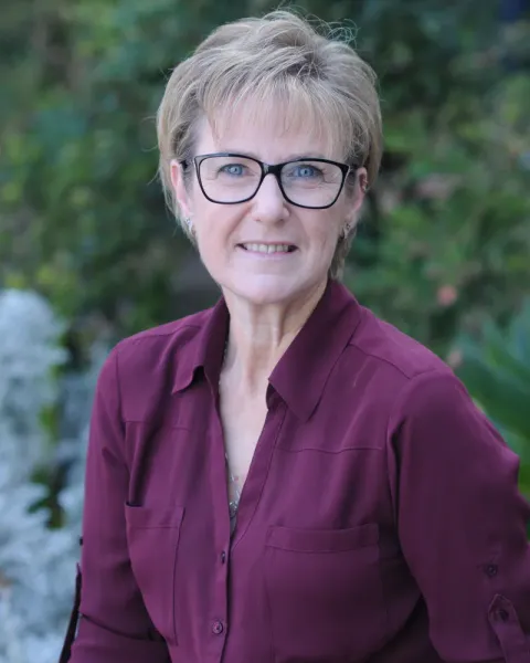 Portrait of Kate Spitzer, smiling, wearing glasses and a maroon shirt, outdoors
