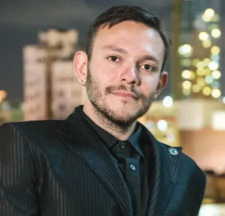 Portrait of Maksim Pecherskiy, with a short beard, in a dark jacket against a city skyline at night