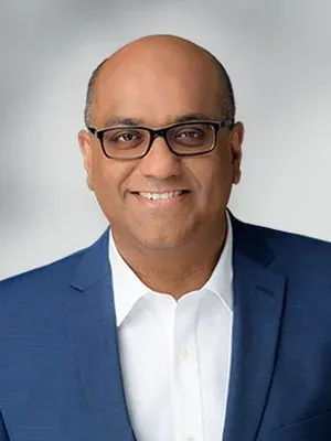 Portrait of Nishal Mohan, smiling, wearing glasses and a blue blazer